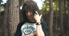 a man wearing a shirt that says hellfire club is standing in the woods