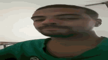 a man with a beard is wearing a green shirt and looking down at the camera .