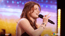 a woman is singing into a microphone with the nbc logo in the background