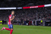 a soccer player in a red and white striped uniform is running on the field .