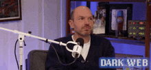 a man sitting in front of a microphone with the words dark web on the bottom right
