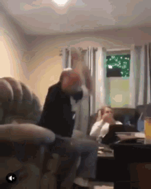 a man is sitting on a couch in a living room while another man sits in a chair