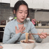 a woman in a blue shirt is eating noodles with chopsticks