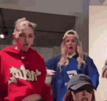 a group of women are standing next to each other in a room . one of the women is wearing a red hoodie .