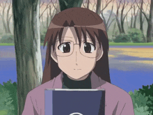 a girl with glasses is holding a book in front of a tree