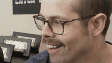 a man wearing glasses and a mustache smiles in front of a sign that says catch