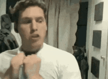 a man in a white shirt is standing in front of a mirror adjusting his tie .