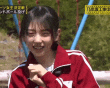 a young woman in a red jacket is smiling while sitting on a swing .
