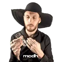 a man wearing a black hat is holding a glass with the word mcdh on the bottom right