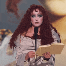 a woman with red hair is speaking into a microphone while holding a book