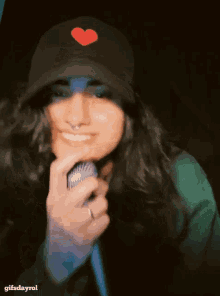 a woman wearing a hat with a red heart on it holds a microphone