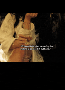 a woman in a white robe is holding a glass of wine with a quote in another language
