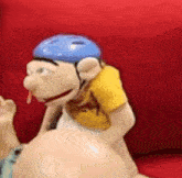 a puppet wearing a blue helmet is sitting on a couch .