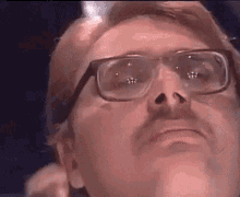 a man wearing glasses and a mustache is looking up at something .