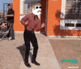 a man in a red shirt and black pants is dancing in front of an orange building