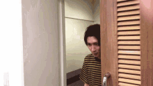 a man in a striped shirt is peeking through a door