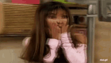 a woman in a pink shirt is covering her face with her hands .