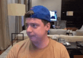 a man wearing a blue hat and a brown shirt looks at the camera in a living room