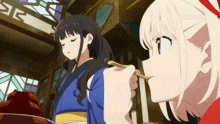 a woman in a blue kimono is being spoon fed by another woman