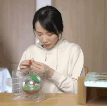 a woman in a white hoodie is opening a plastic container with a green plant in it