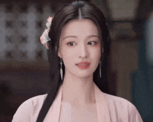 a woman with long hair and a flower in her hair is wearing a pink shirt and earrings .