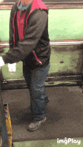 a man wearing a black jacket and a red vest is standing in front of a green wall with imgplay written on the bottom
