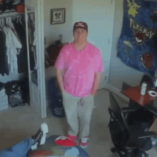 a man in a pink shirt stands in a room with a pokemon tapestry on the wall