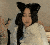 a woman wearing black cat ears is holding a small white dog