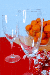 two wine glasses sitting on a table next to a bowl of oranges and lindt candies