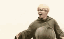 a man with blonde hair is covering his mouth with his hands and laughing .