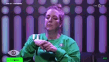 a woman in a green sweater is sitting in front of a purple wall