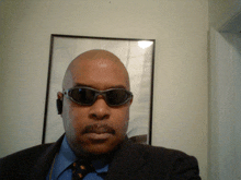 a man wearing sunglasses and a suit is taking a selfie