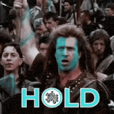 a man with blue paint on his face is holding a sword in front of a crowd of people and the word hold is above him