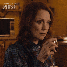 a woman drinking a glass of wine with a son of a grifch logo in the background