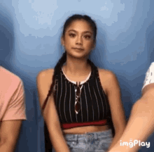a woman in a striped crop top is sitting in front of a blue wall