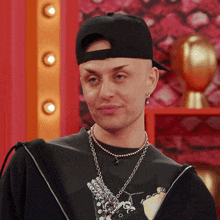 a man wearing a baseball cap and a necklace is looking at the camera