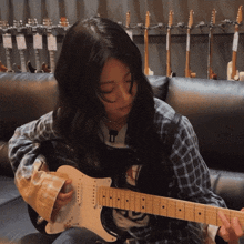 a woman is playing a guitar in front of a row of guitars