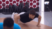 a man in a black shirt is doing push ups on a wooden floor in a gym