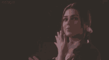 a woman is smiling and clapping her hands in front of a black background .