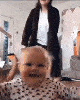 a woman is standing next to a baby who is making a face .