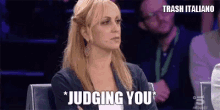 a woman is sitting in a chair with her arms crossed and the words judging you .