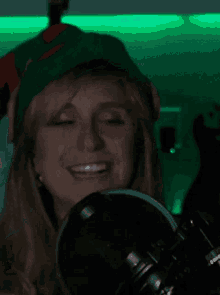 a woman wearing a green elf hat is smiling while holding a microphone