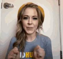 a woman wearing a hat and a t-shirt is standing in front of a door and making a funny face .