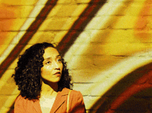 a woman with curly hair is standing in front of a yellow wall