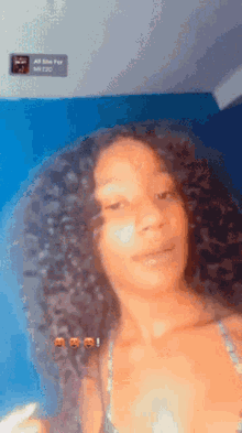 a girl with curly hair is standing in front of a blue wall and looking at the camera .