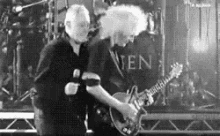 a black and white photo of two men playing guitars on stage .