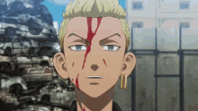 a man with blood on his face and a pile of cars in the background