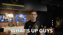 a man standing in a room with the words what 's up guys behind him