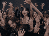 a woman in a black dress is surrounded by other women raising their hands in the air