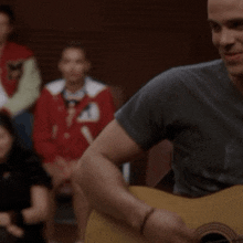 a man is playing a guitar in front of a group of people wearing varsity jackets with the letter m on the sleeves